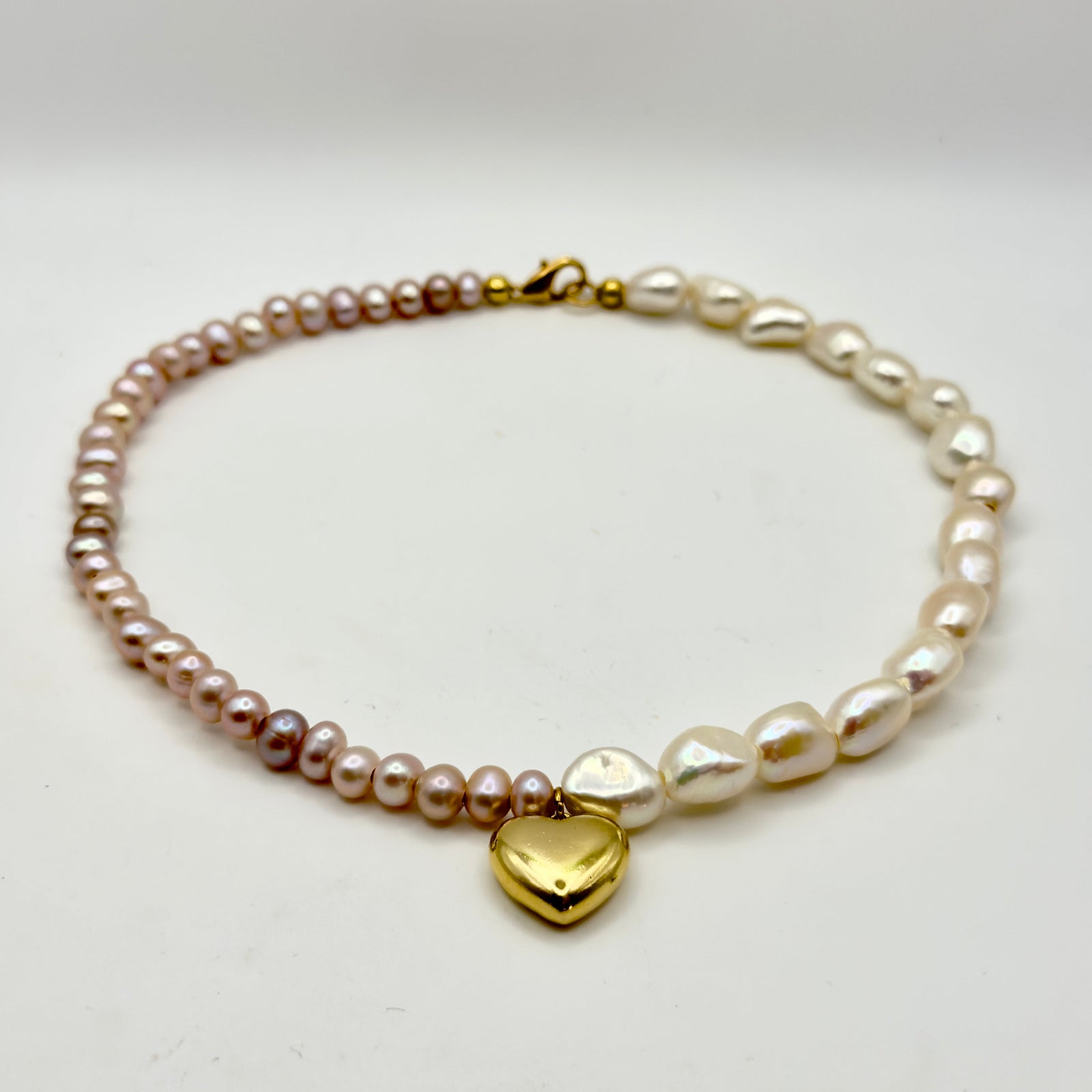 18 inch asymmetrical necklace with half pink pearls and half white baroque pearls divided by a gold heart charm.