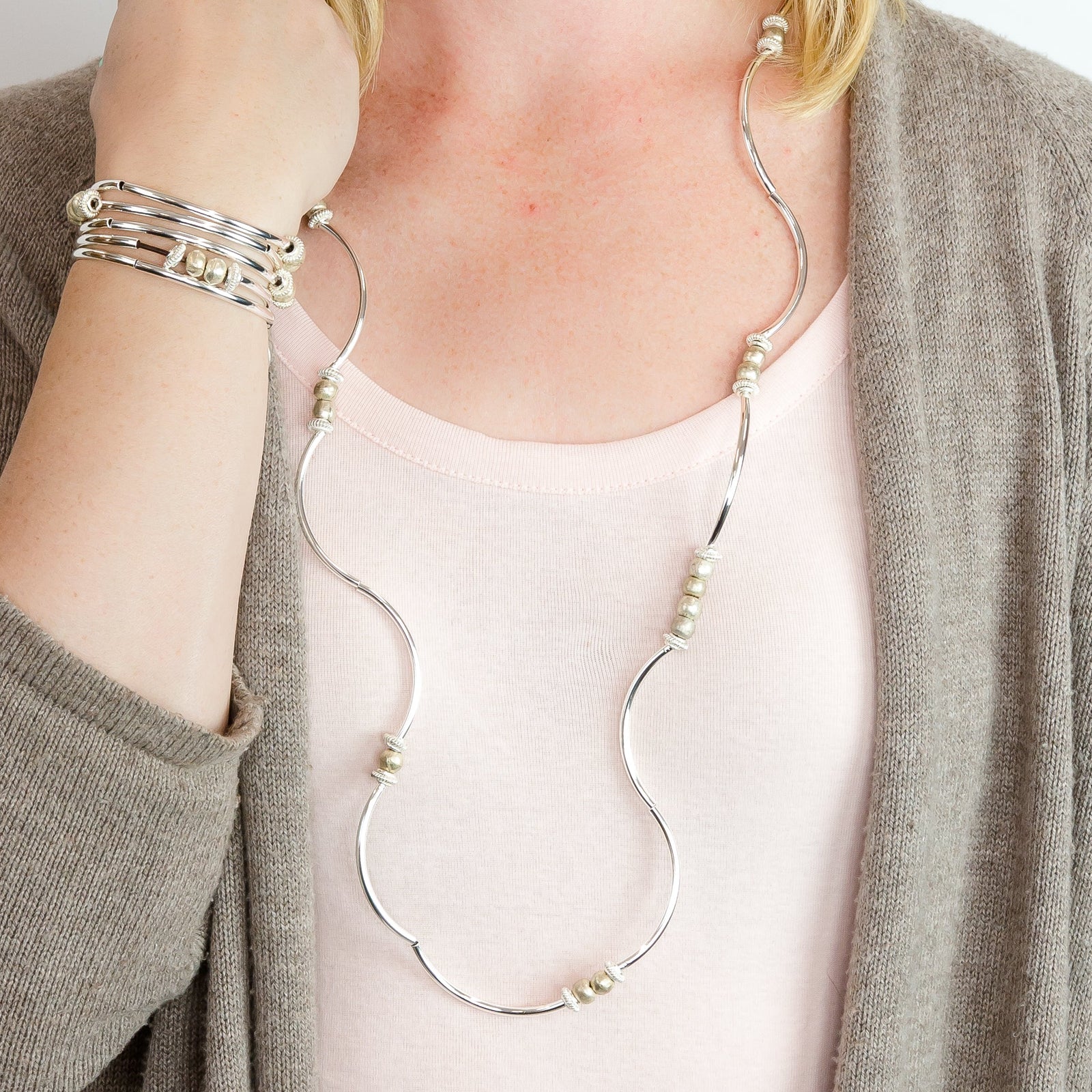Person wearing a long necklace and multiple bracelets on a plain background