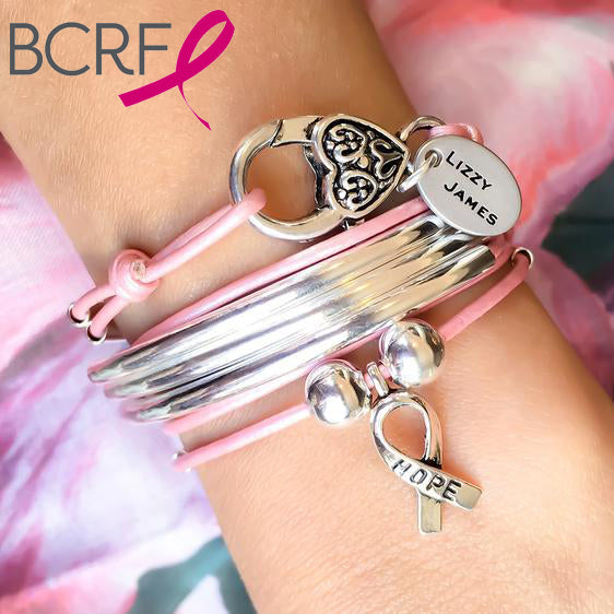 Silver and pink bracelets on a wrist with a 'HOPE' charm against a fluffy white background