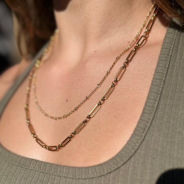 Close-up of a person wearing two gold necklaces on a plain background