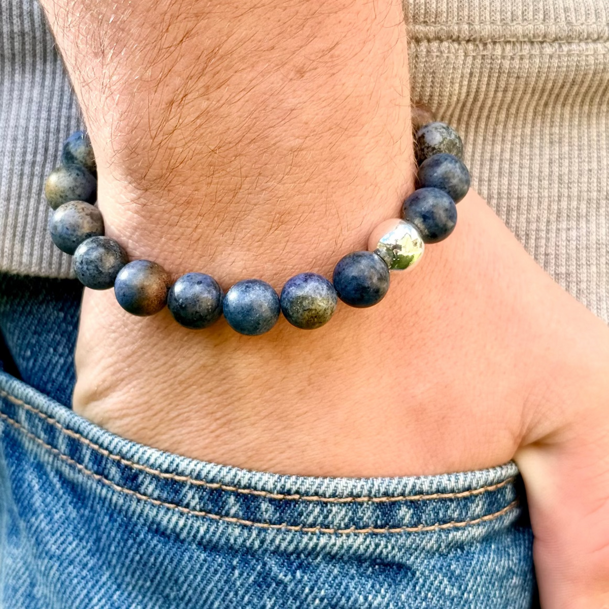 Person wearing a blue beaded bracelet on a wrist with a neutral background