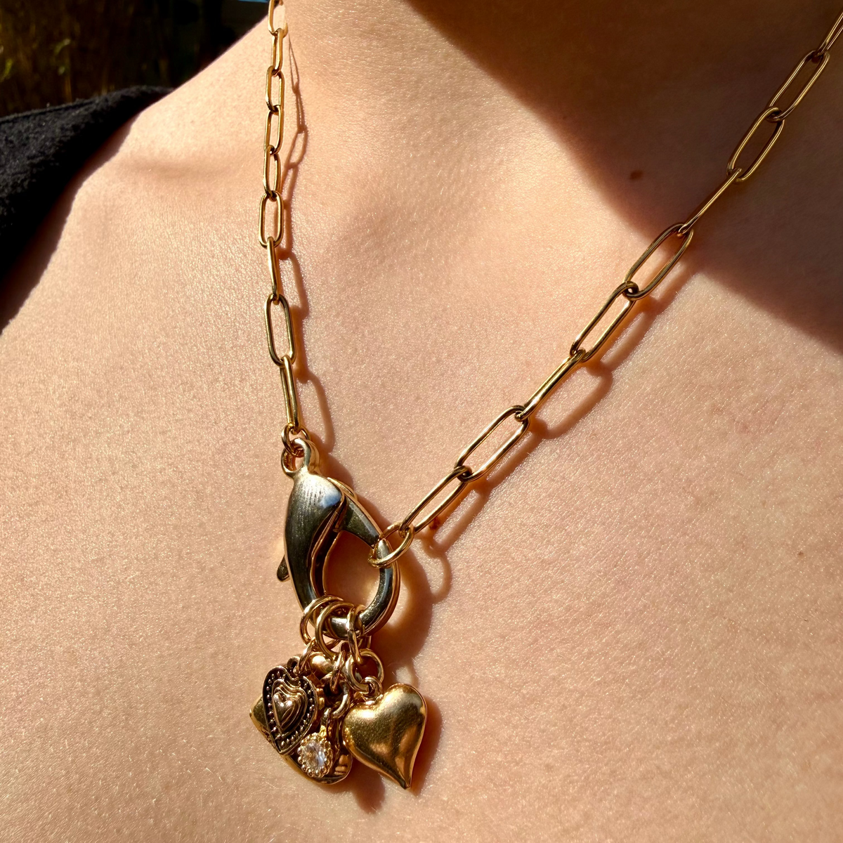 Gold necklace with heart-shaped charms on a person's neck against a blurred natural background