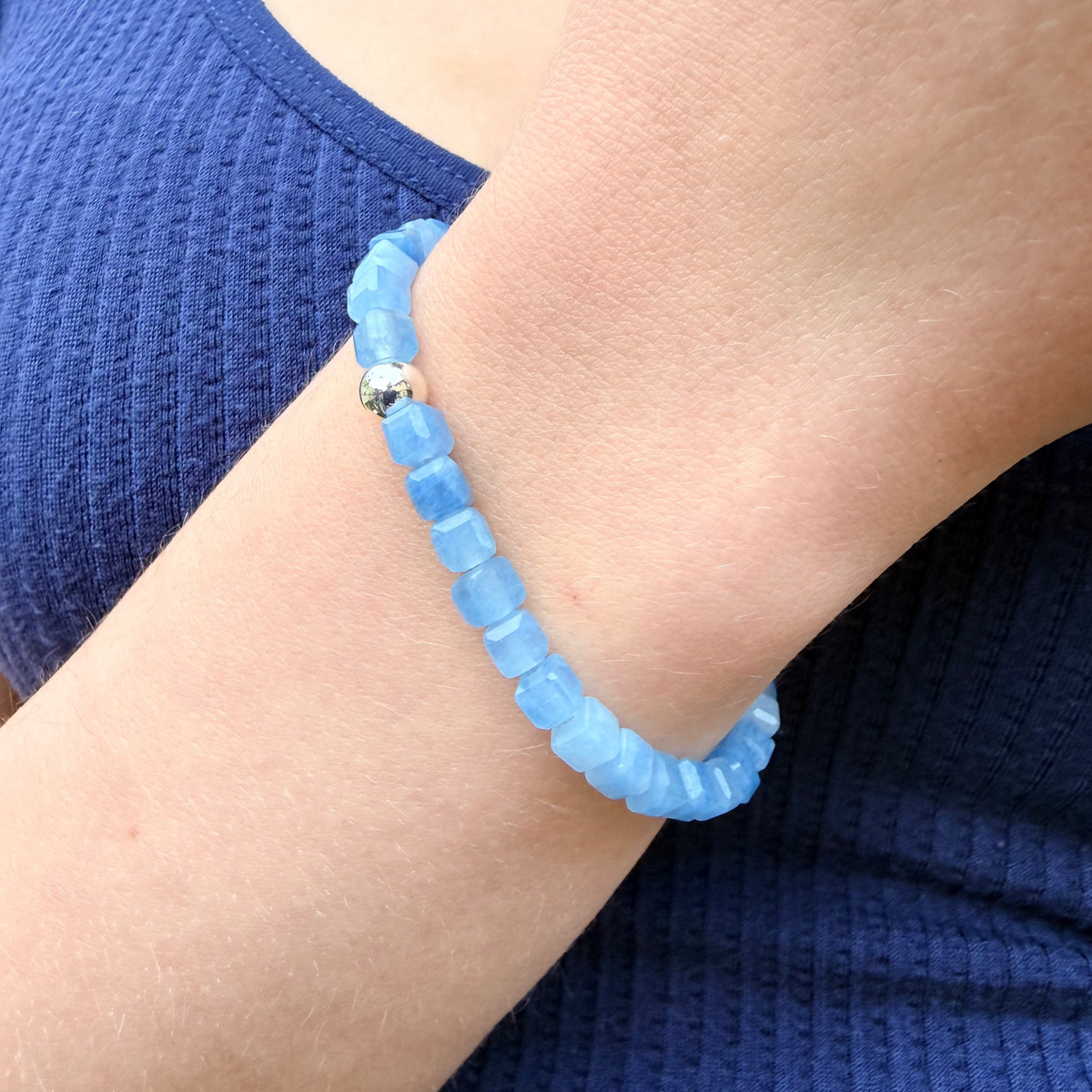 Blue beaded bracelet on a wrist with a blue top