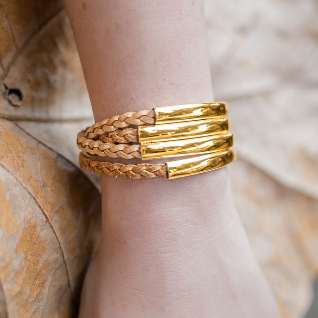 Gold and braided leather bracelet on a wrist with a blurred background