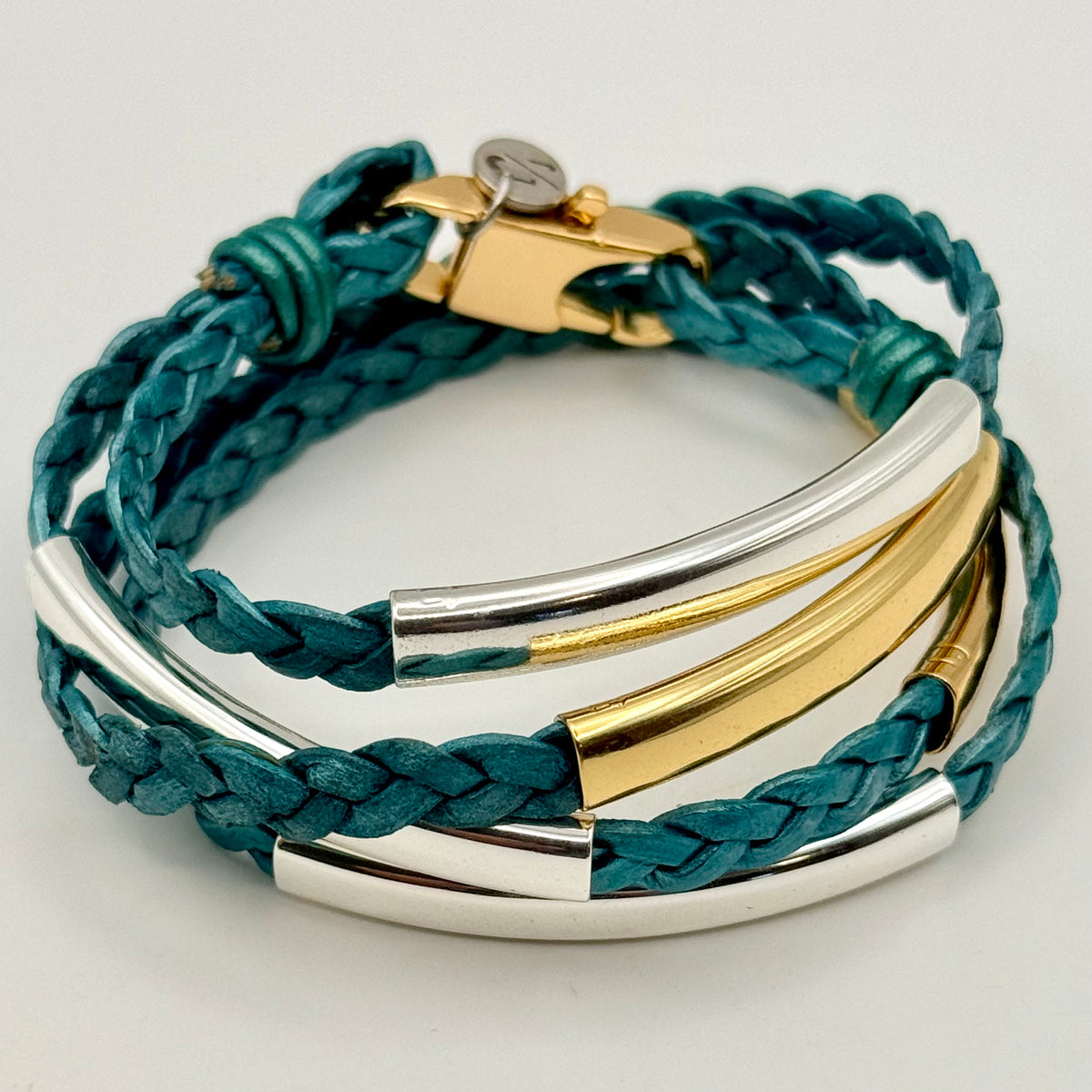 A multi-strand wrap bracelet featuring dark teal braided leather cords and polished metal accents in gold and silver, displayed on a clean white background.