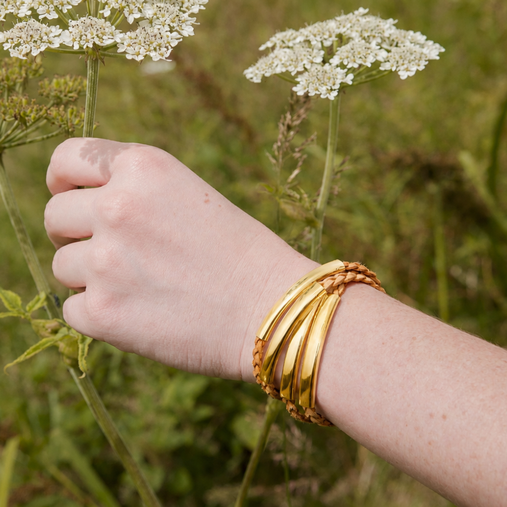 Hand wearing a gold bracelet in a natural setting with flowers