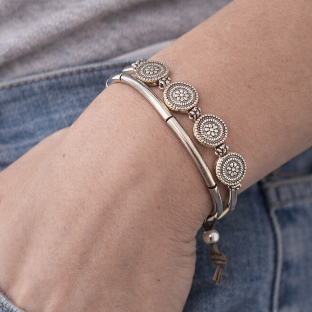 Close-up of a wrist wearing a silver bracelet with intricate designs, against a blurred background.