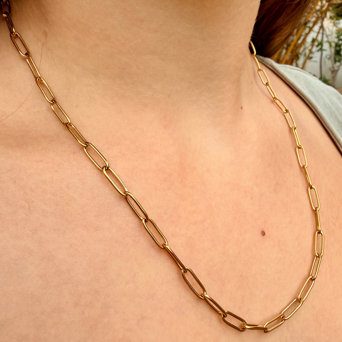 Gold finish paperclip chain necklace around a womans neck.