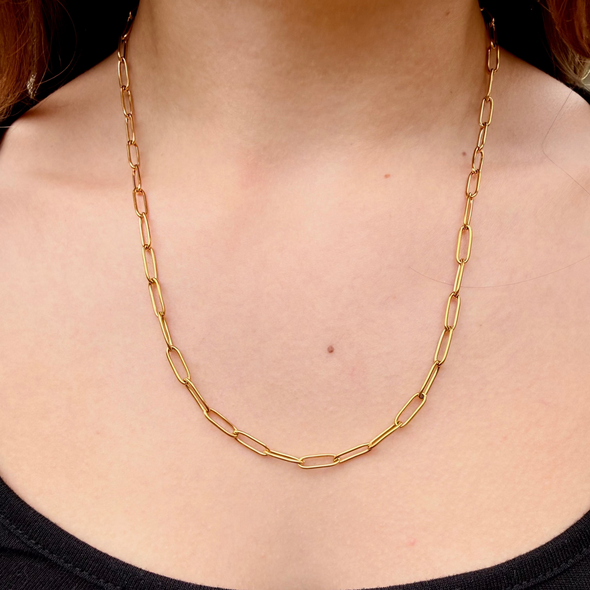 Gold chain necklace worn by a person against a black background