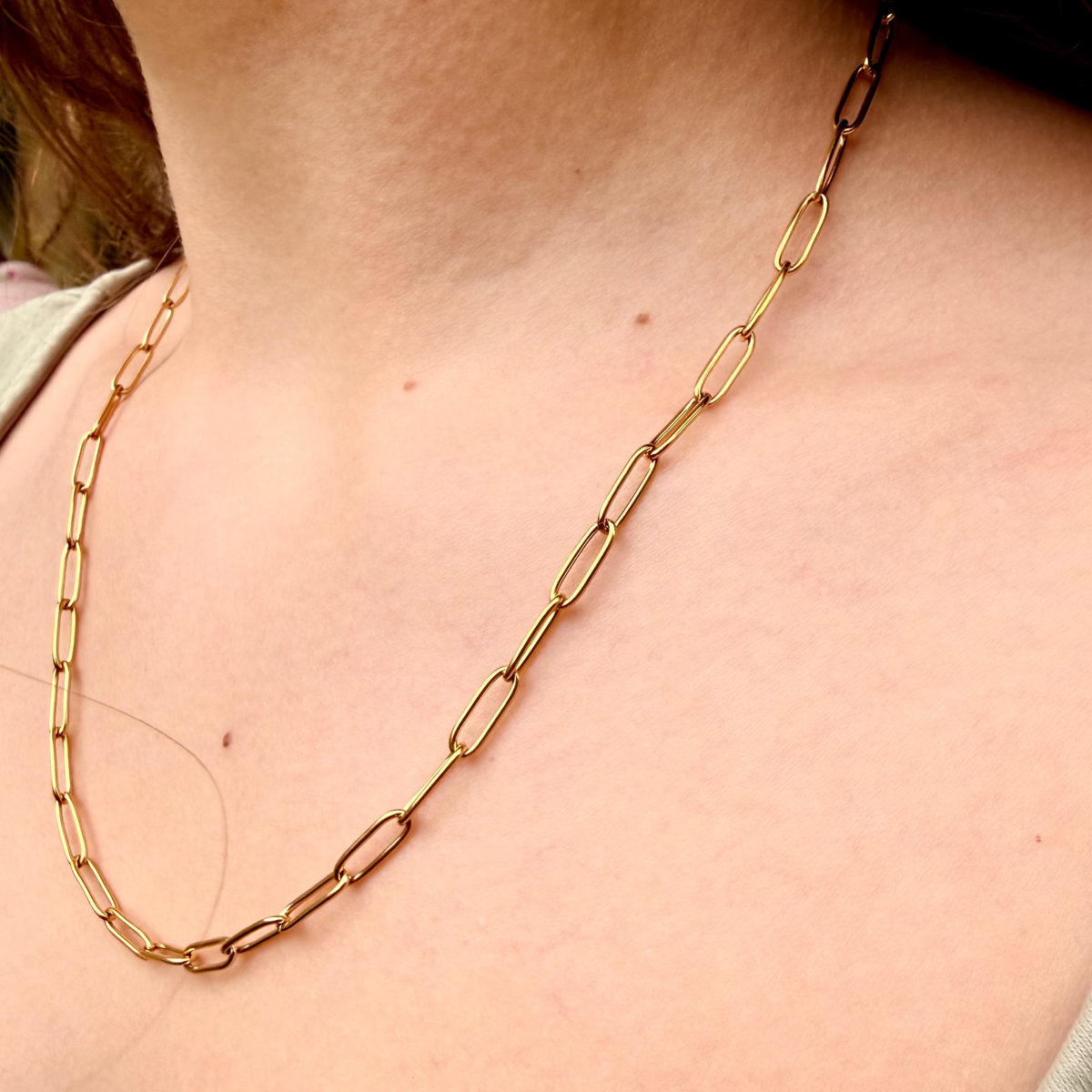 Gold chain necklace on a person's neck with a neutral background