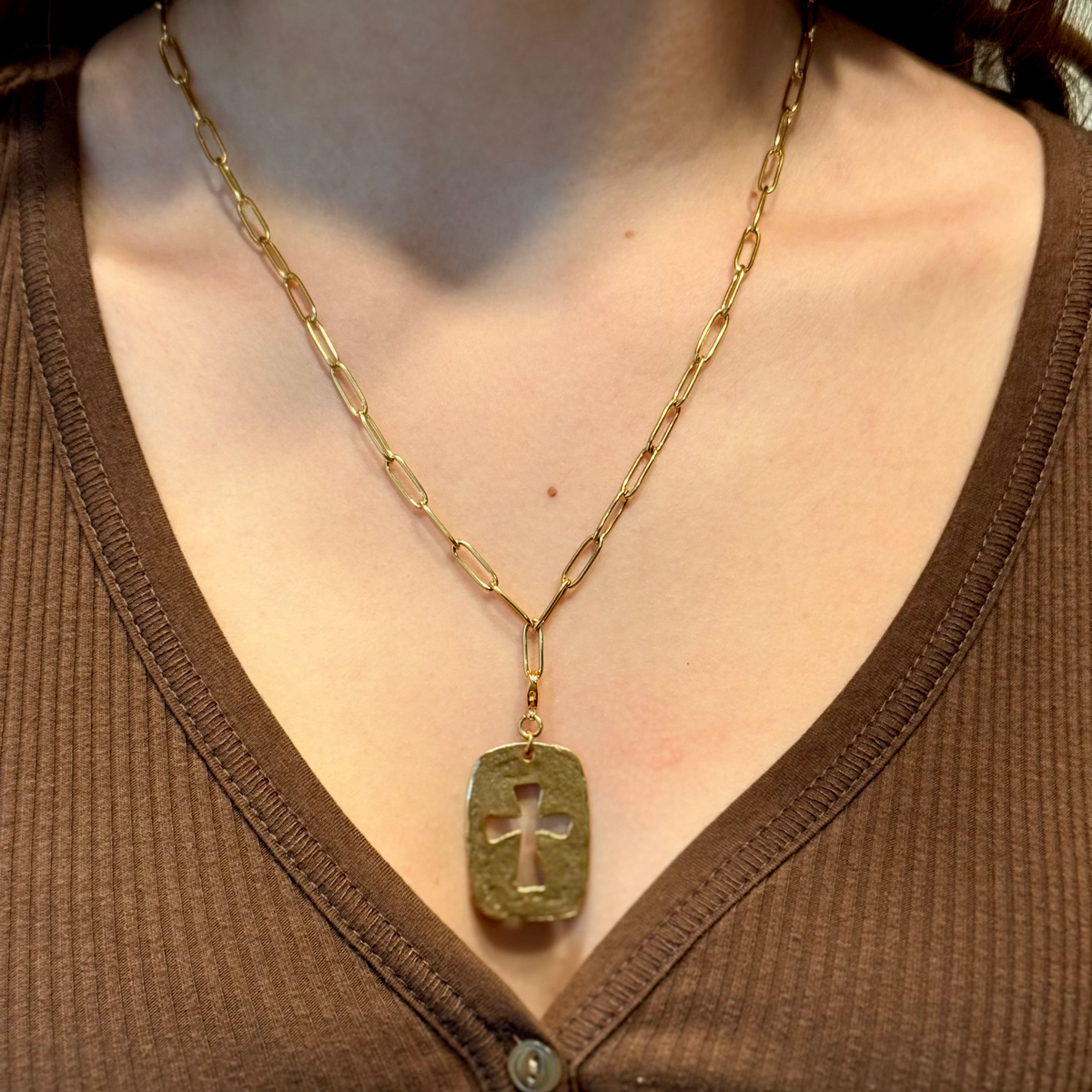 Gold necklace with a cross pendant on a person wearing a brown shirt.