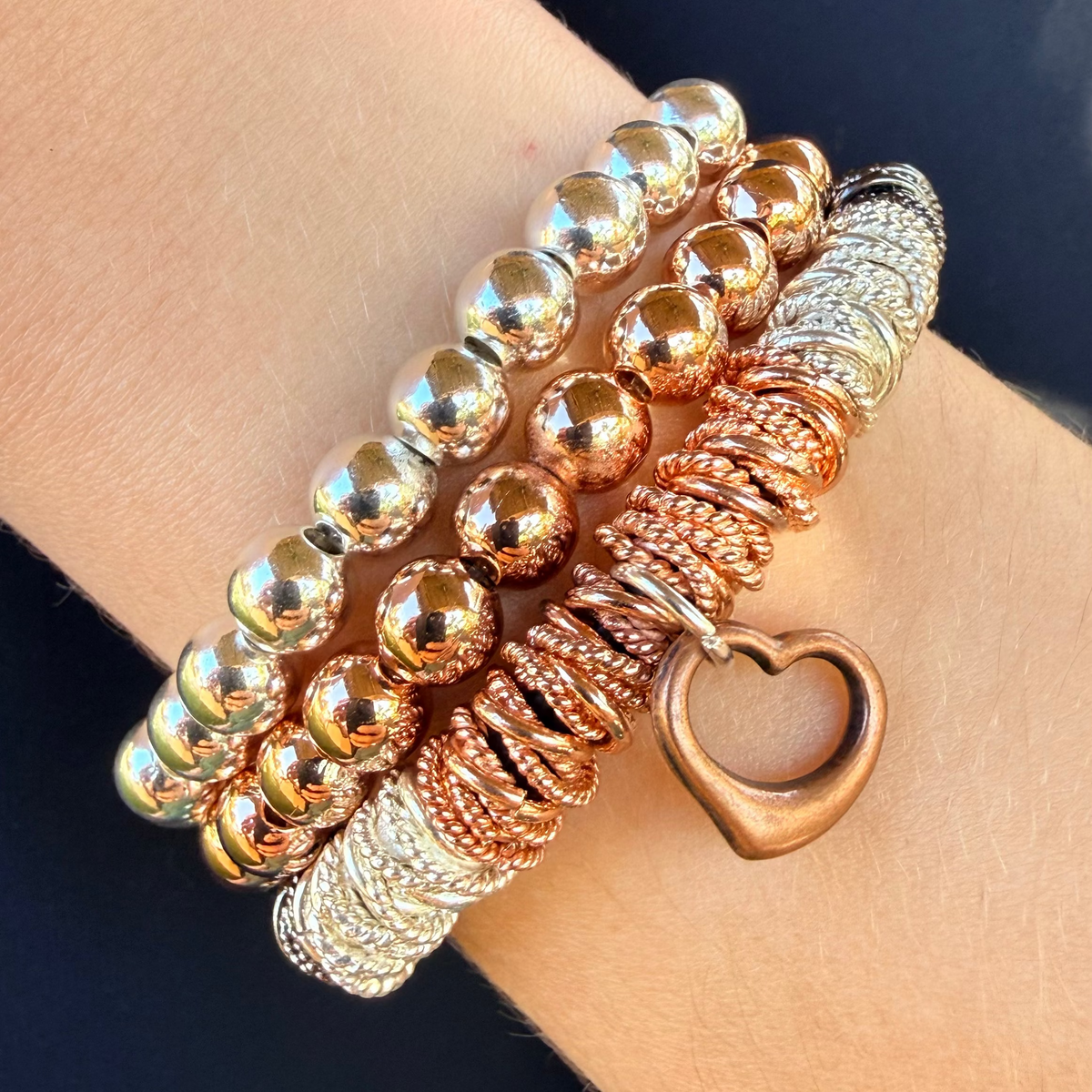 Three gold bracelets on a wrist against a dark background