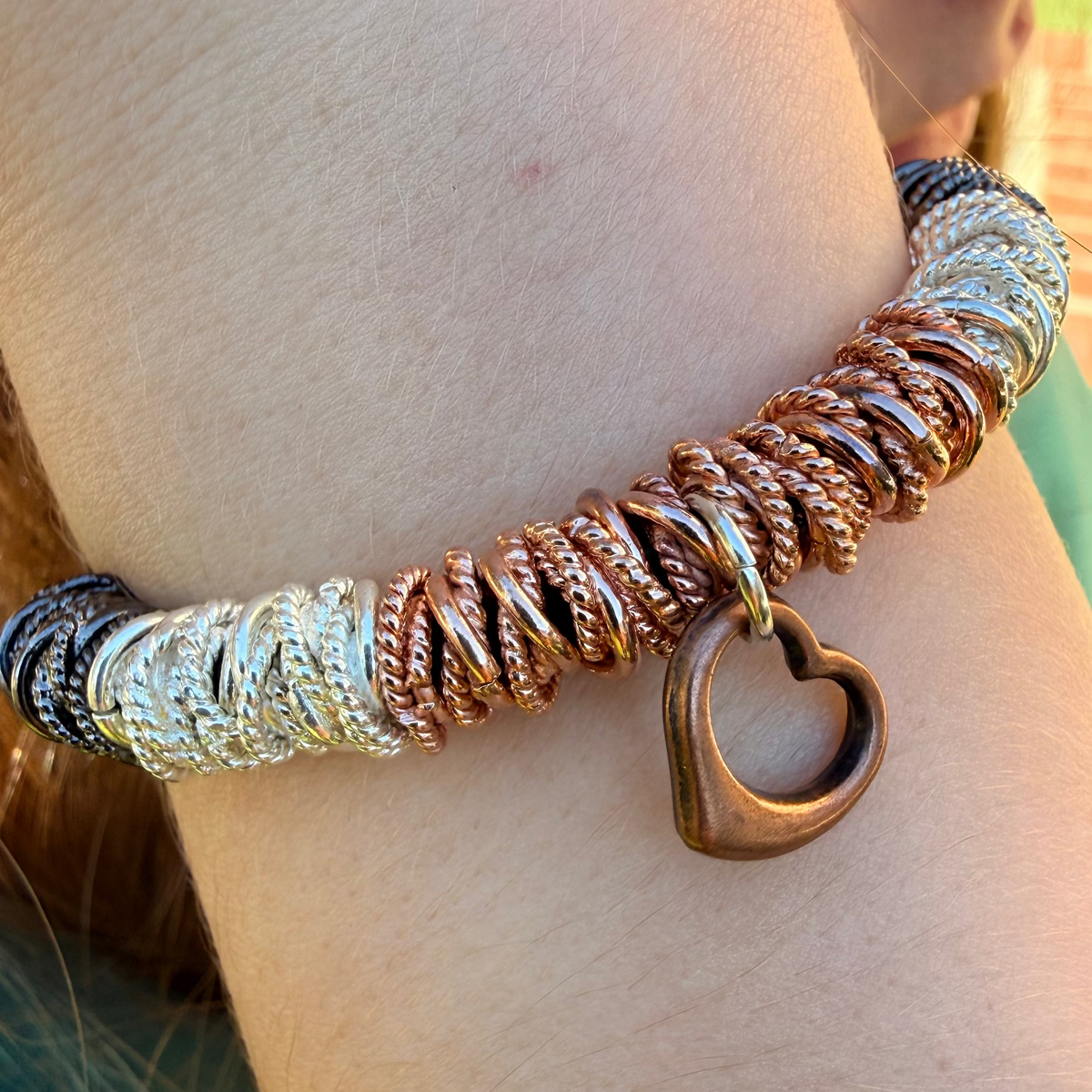 Close-up of a person wearing a multicolored braided bracelet with a heart charm.
