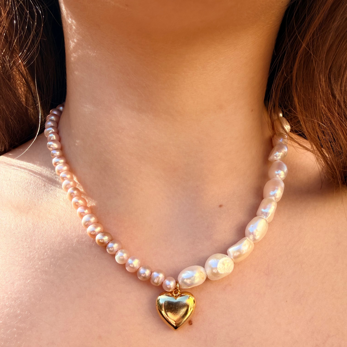 18 inch asymmetrical necklace with half pink pearls and half white baroque pearls divided by a gold heart charm.