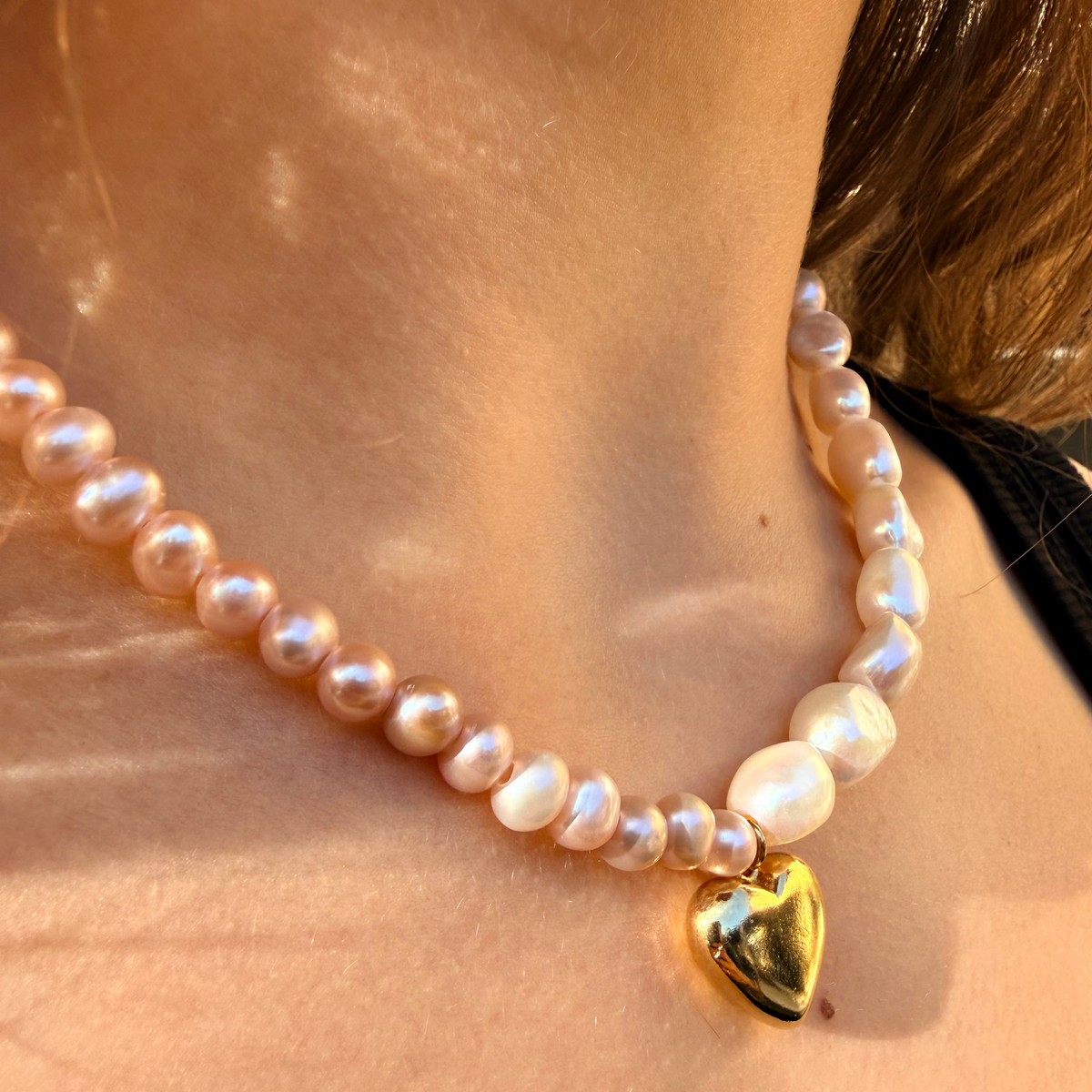 Pearl necklace with a gold heart charm worn by a person