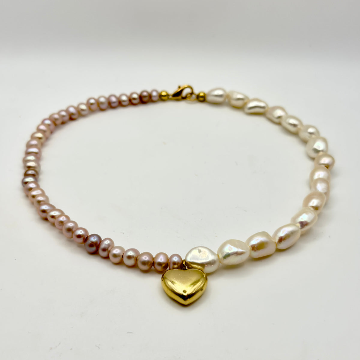 Pearl bracelet with a gold heart charm on a light gray background