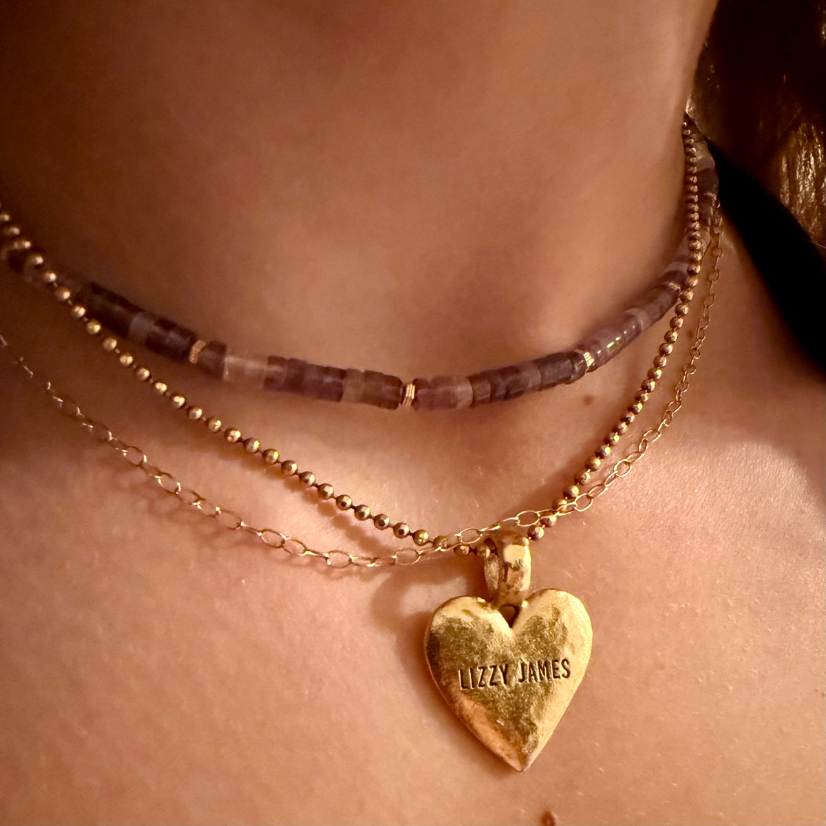Gold heart-shaped necklace with 'Lizzy James' engraving on a person's neck.