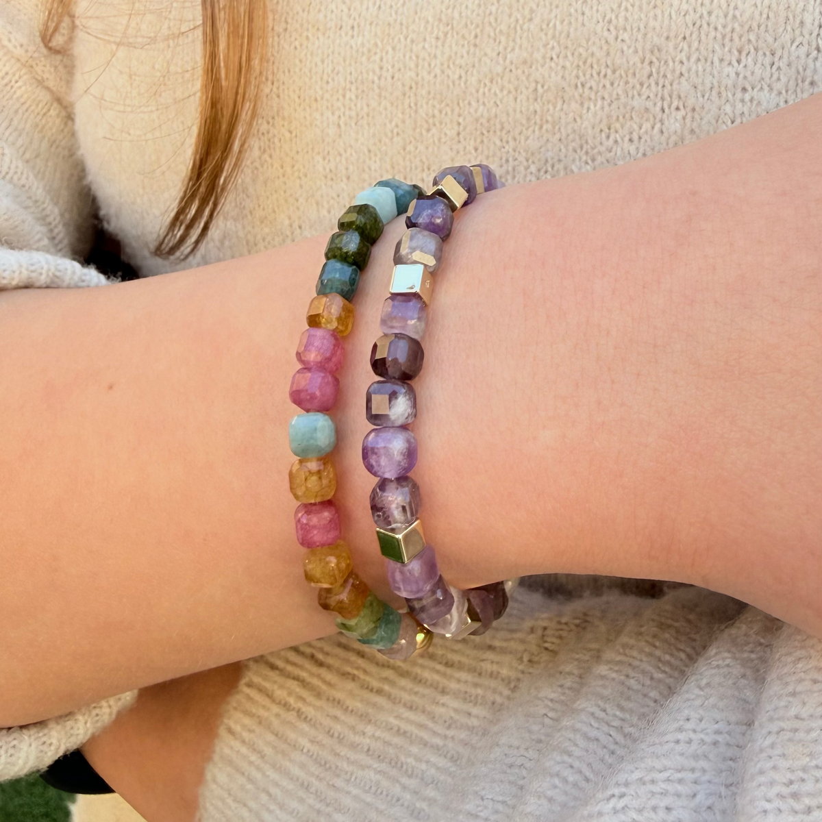 Multicolored beaded bracelets on a person's wrist with a neutral background
