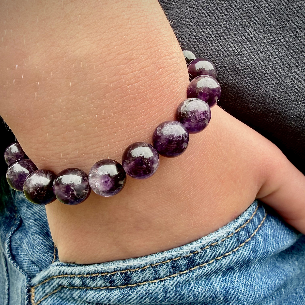 Close-up of a person wearing a purple beaded bracelet on a denim sleeve.