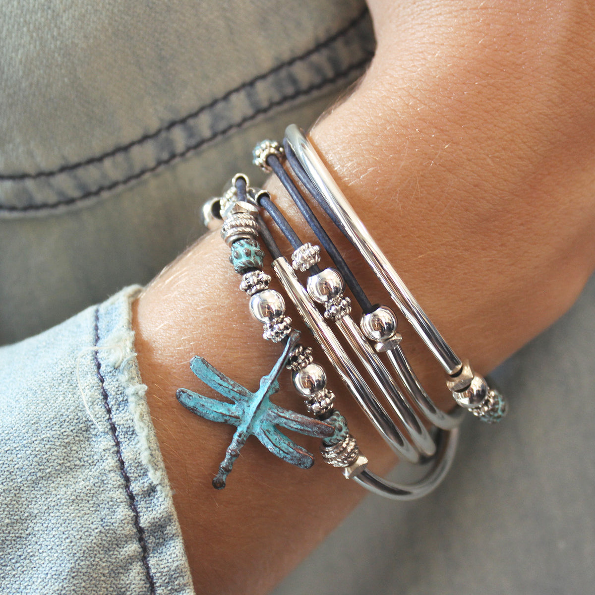 Close-up of a wrist wearing multiple silver bracelets with beads on a denim background