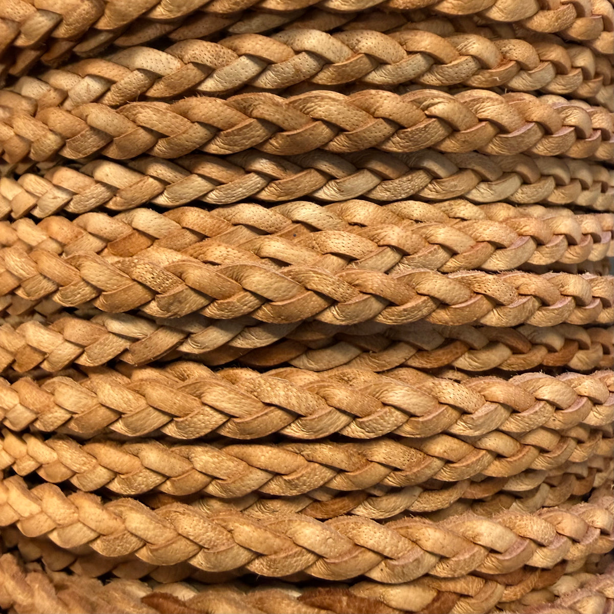 A close-up of thick braided natural fiber rope or cord in warm tan and light brown tones, filling the frame.