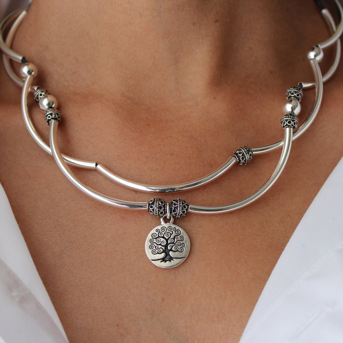 Silver bracelet with a tree of life charm on a person wearing a white shirt.