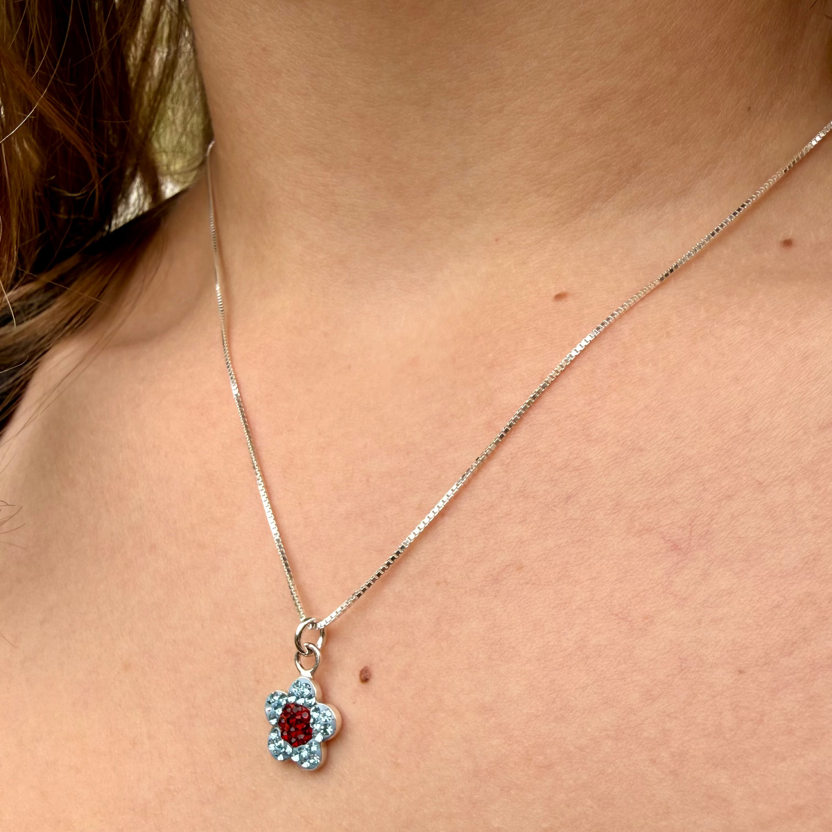 Necklace with a flower-shaped pendant featuring red and blue stones on a person's neck.