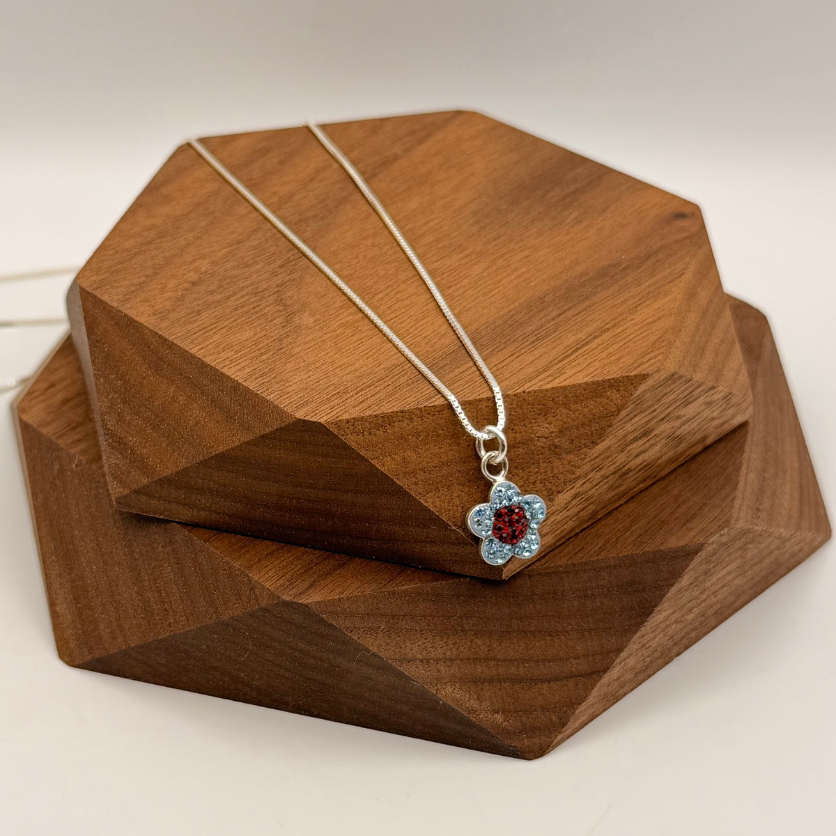 Flower-shaped necklace with red and blue gemstones on a wooden stand