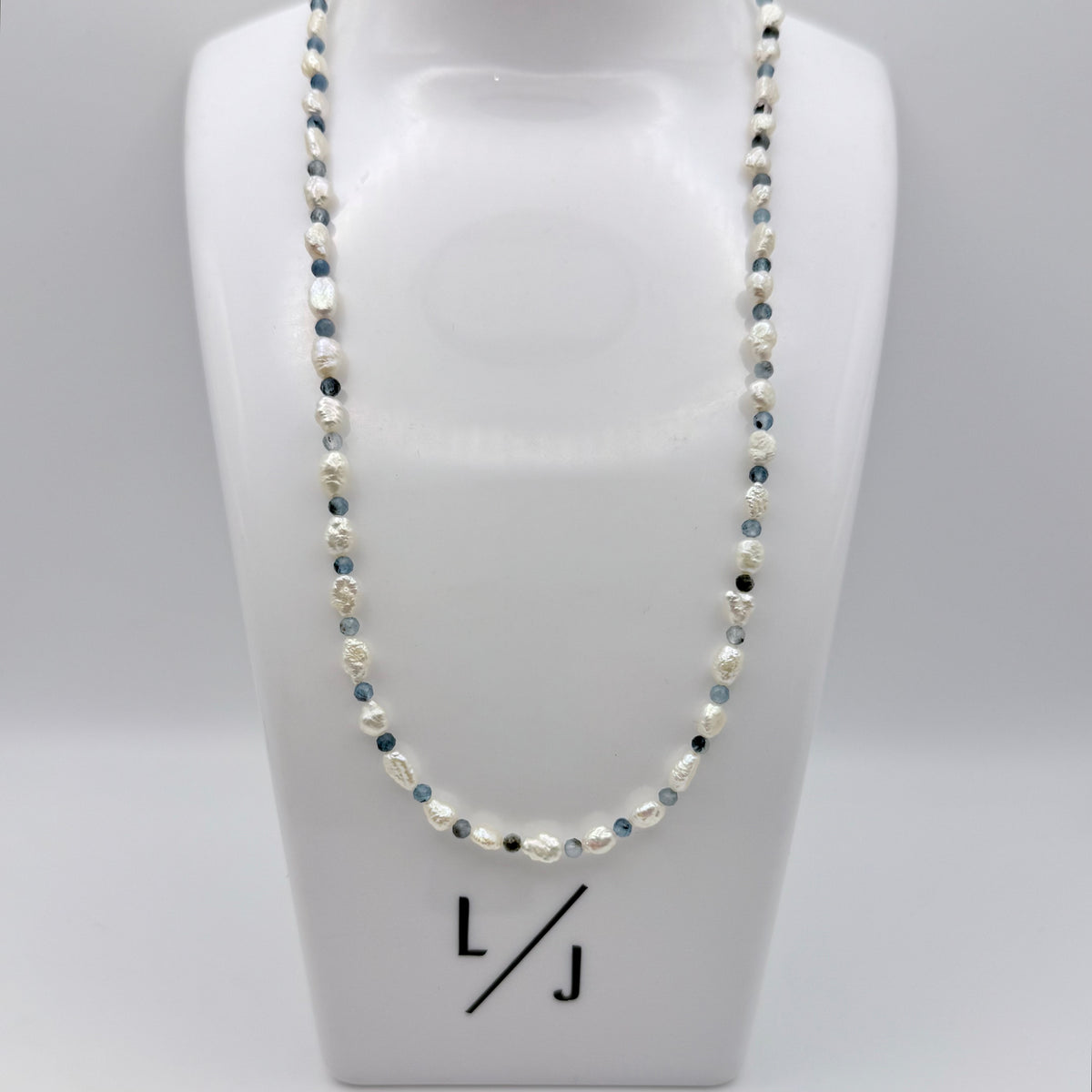 Pearl necklace on a mannequin bust with 'LJ' branding.
