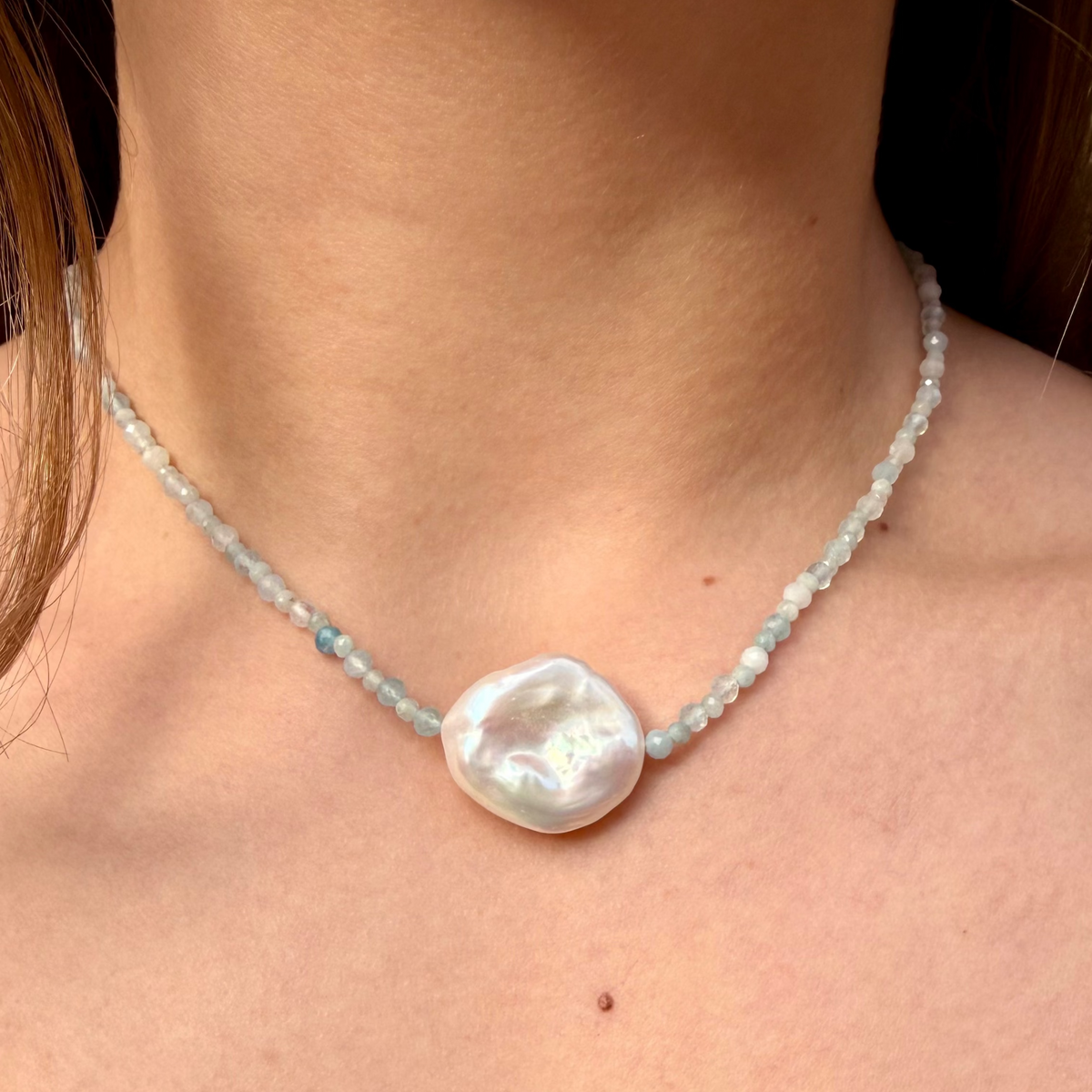 Pearl necklace with a large pearl pendant on a person's neck