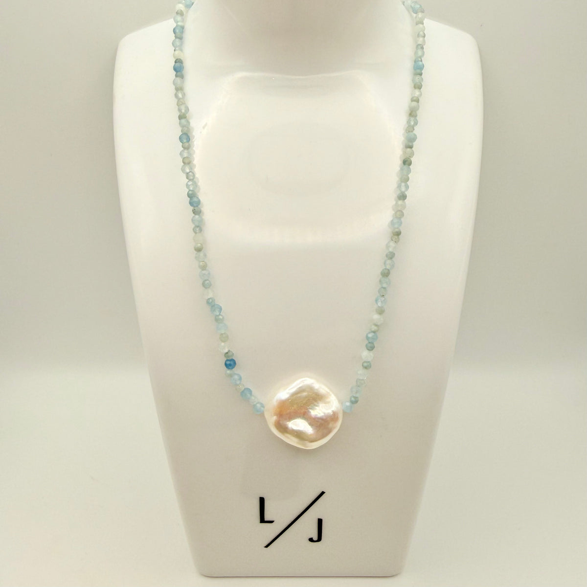 Necklace with a large pearl pendant on a mannequin bust, branded 'LJ'.