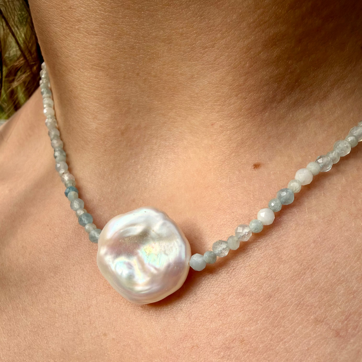 Pearl necklace with a large pearl pendant on a person's neck