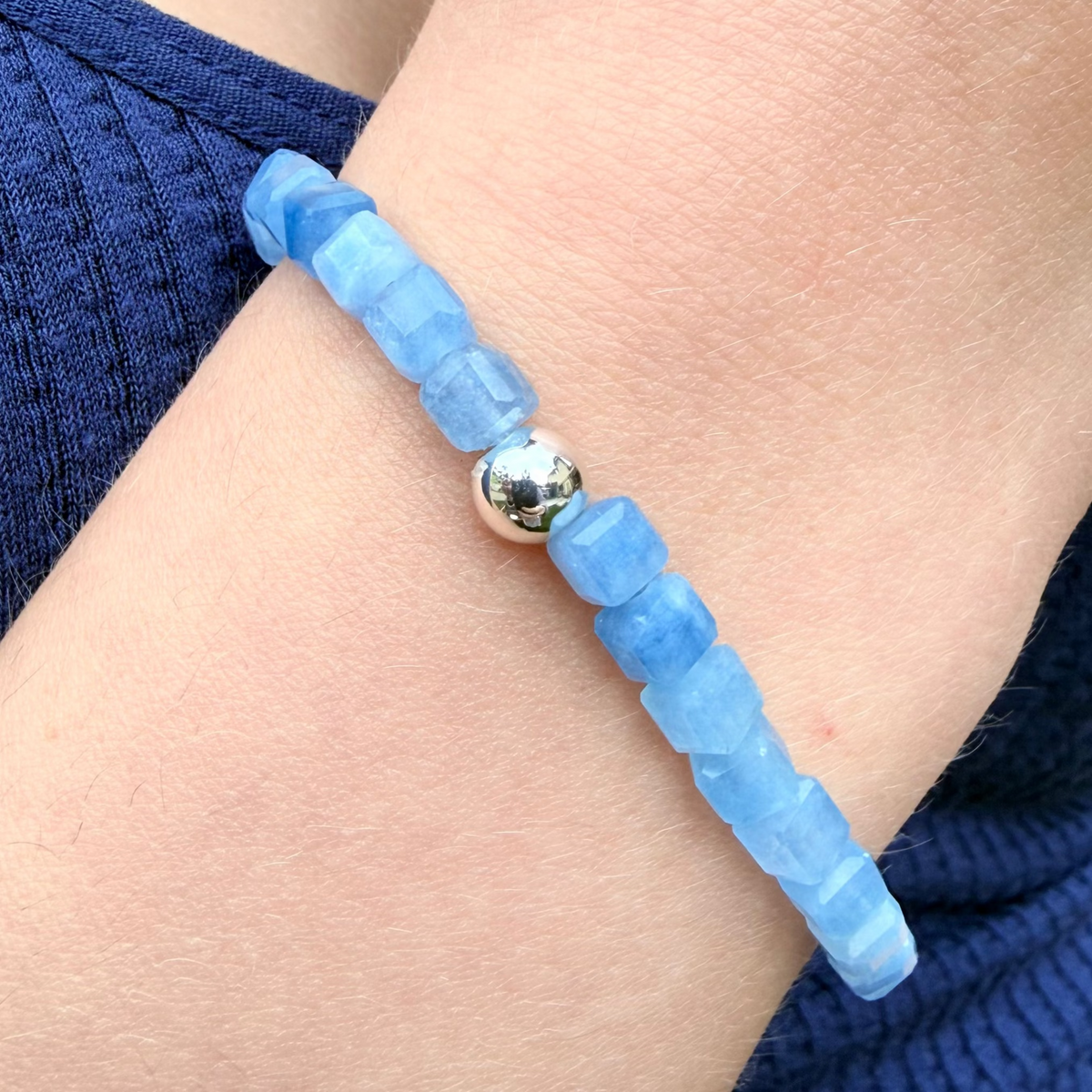 Blue beaded bracelet with a silver bead on a wrist against a blue sleeve.