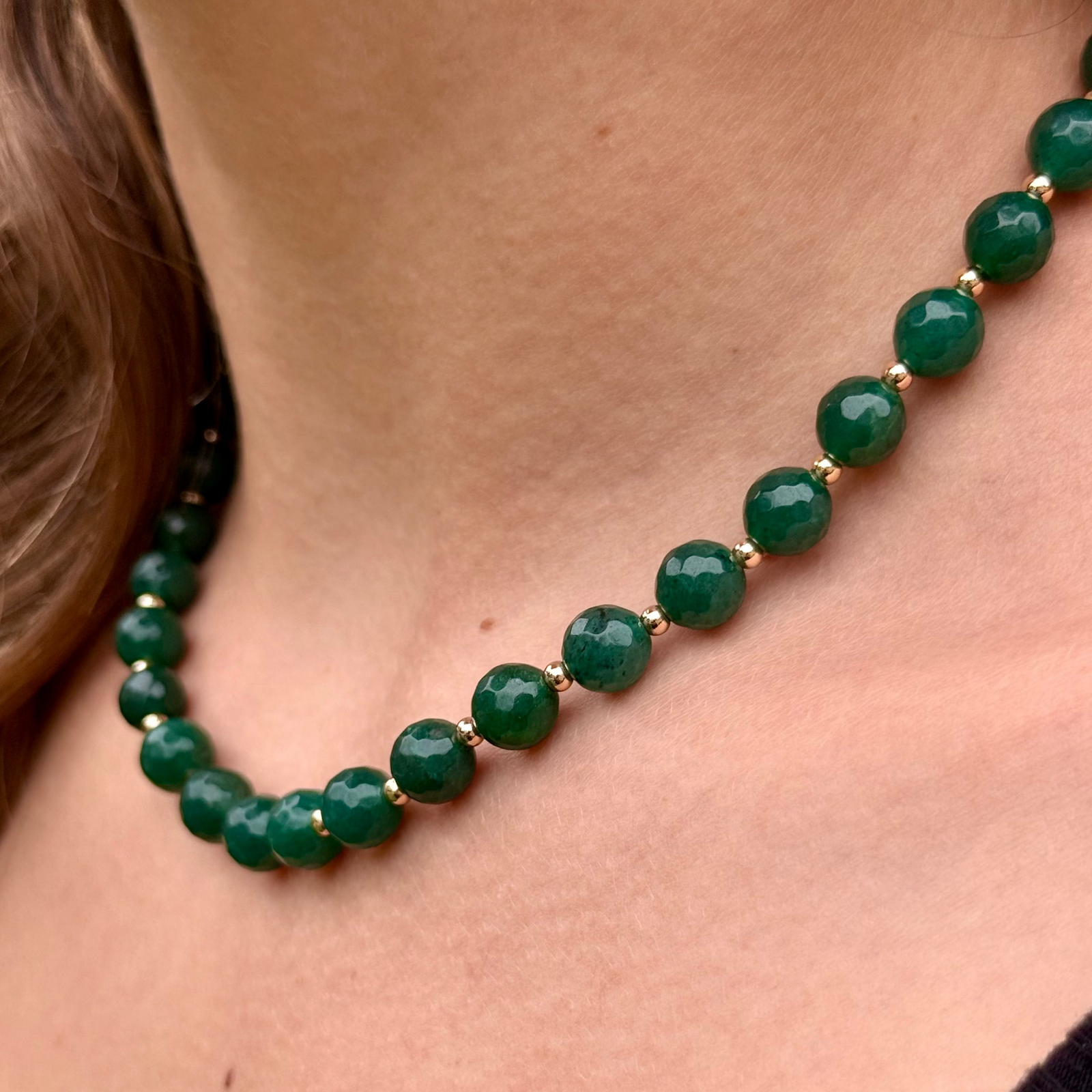 Large green emerald colored jade beads and tiny gold-beaded necklace on woman's neck