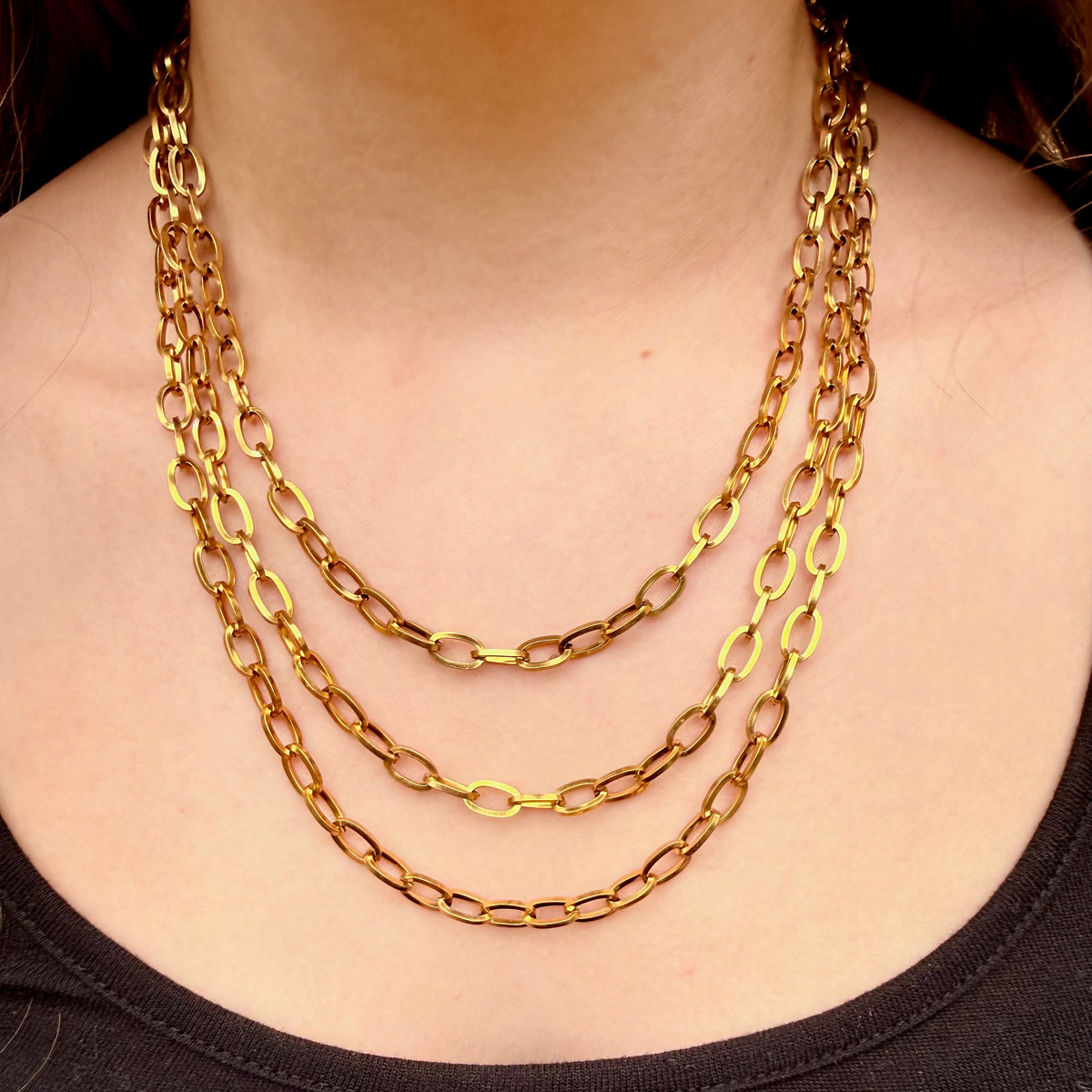 Gold chain necklace on a person wearing a black top against a dark background