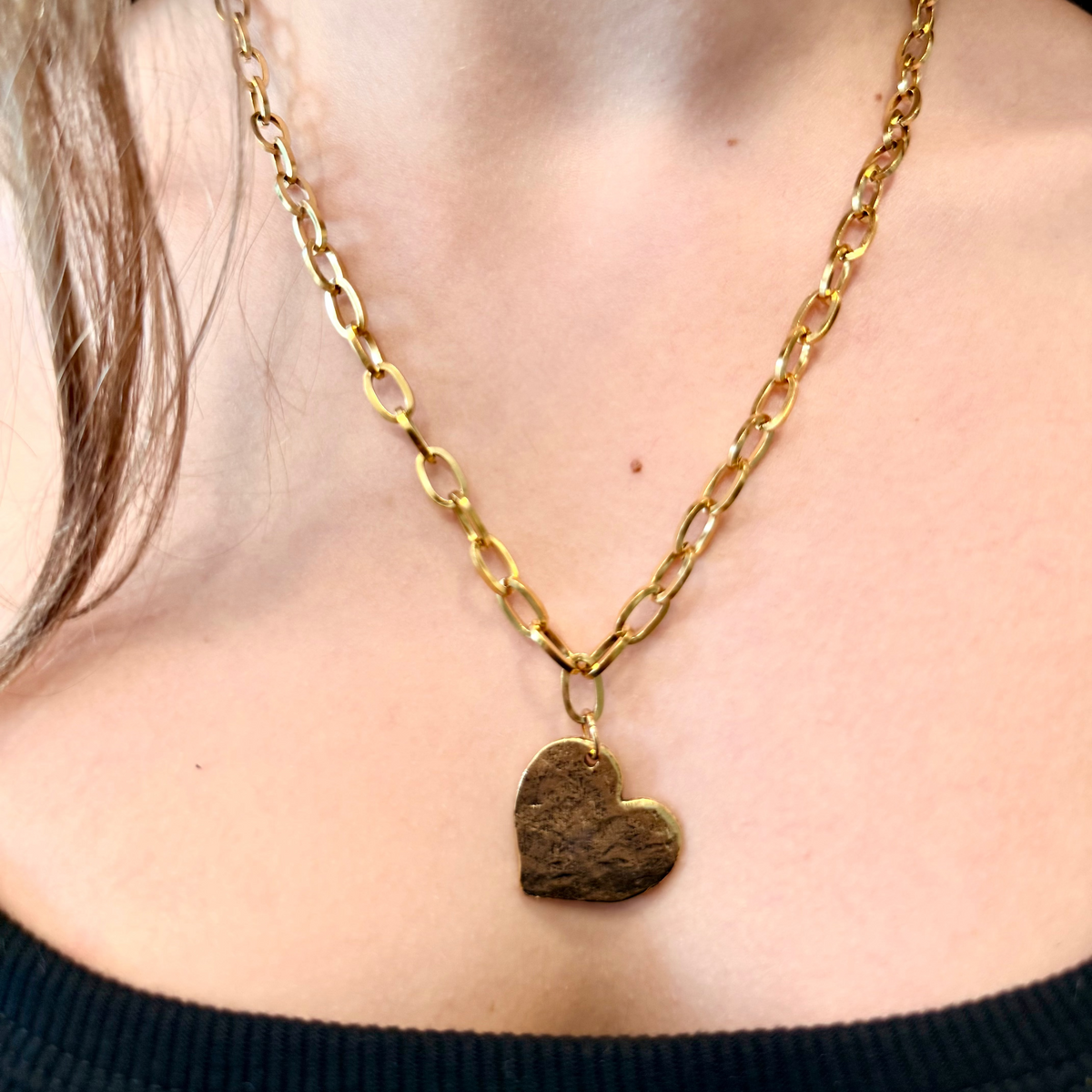 Gold chain necklace with a heart pendant worn by a person