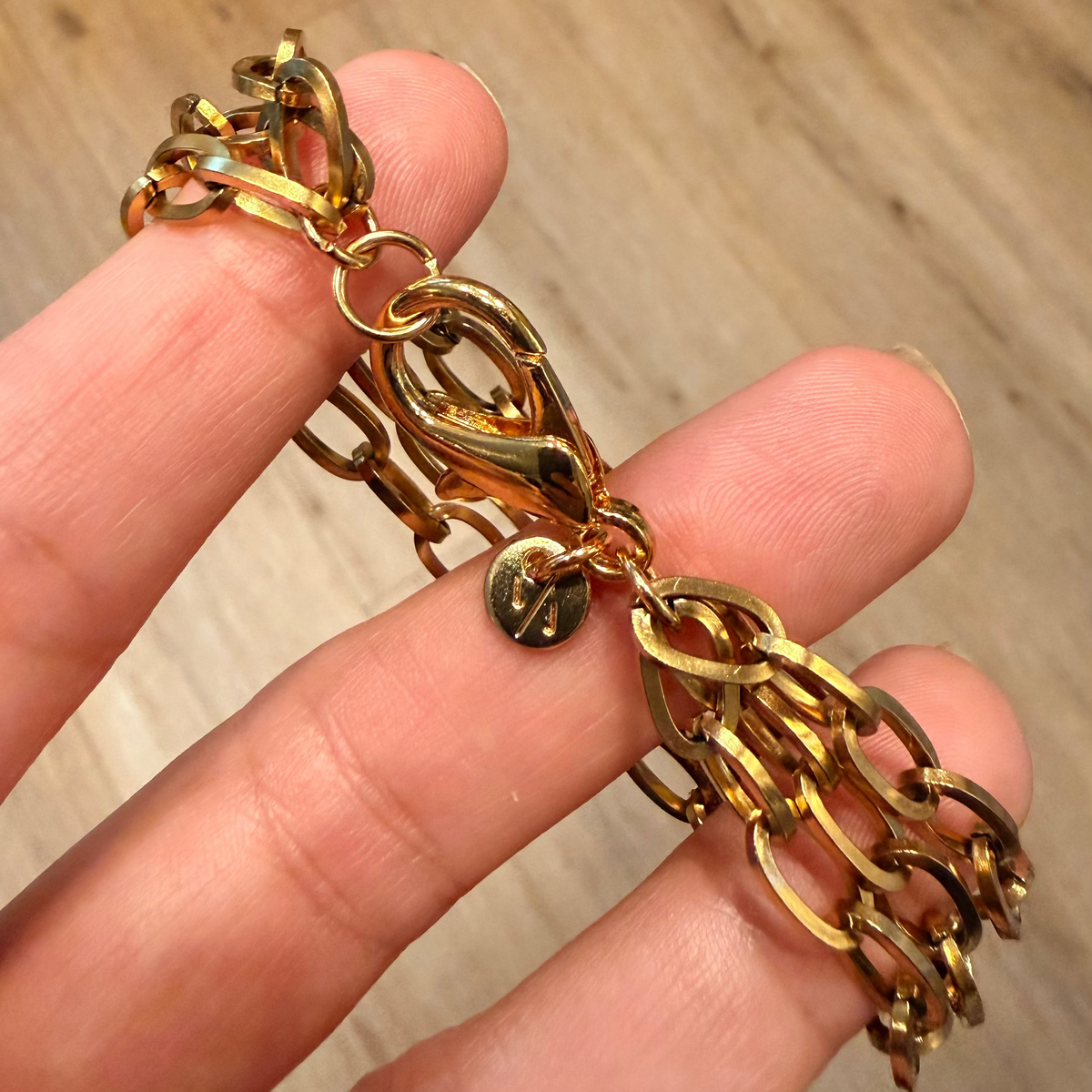 Gold chain bracelet held by a hand on a wooden surface