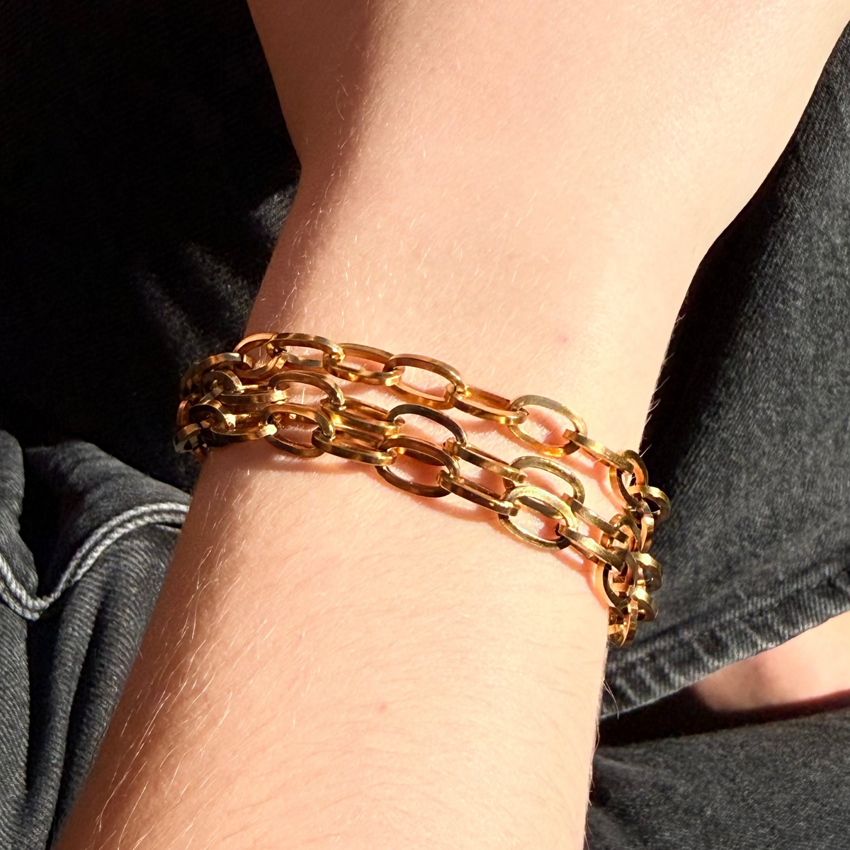 Gold chain bracelet on a wrist with a dark background