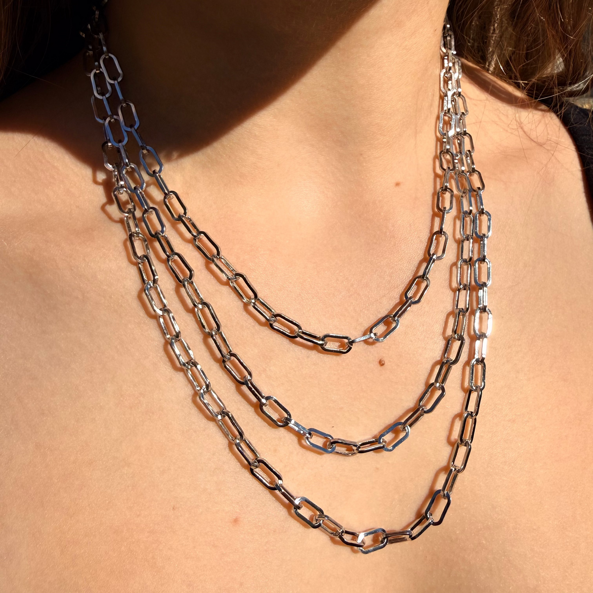 Close-up of a person wearing a layered chain necklace.