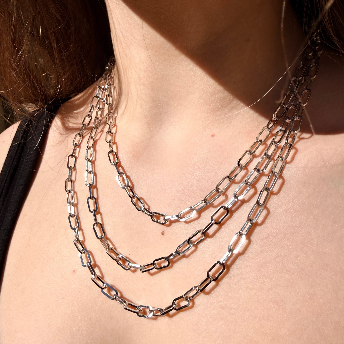 Close-up of a person wearing multiple chain necklaces on a blurred background
