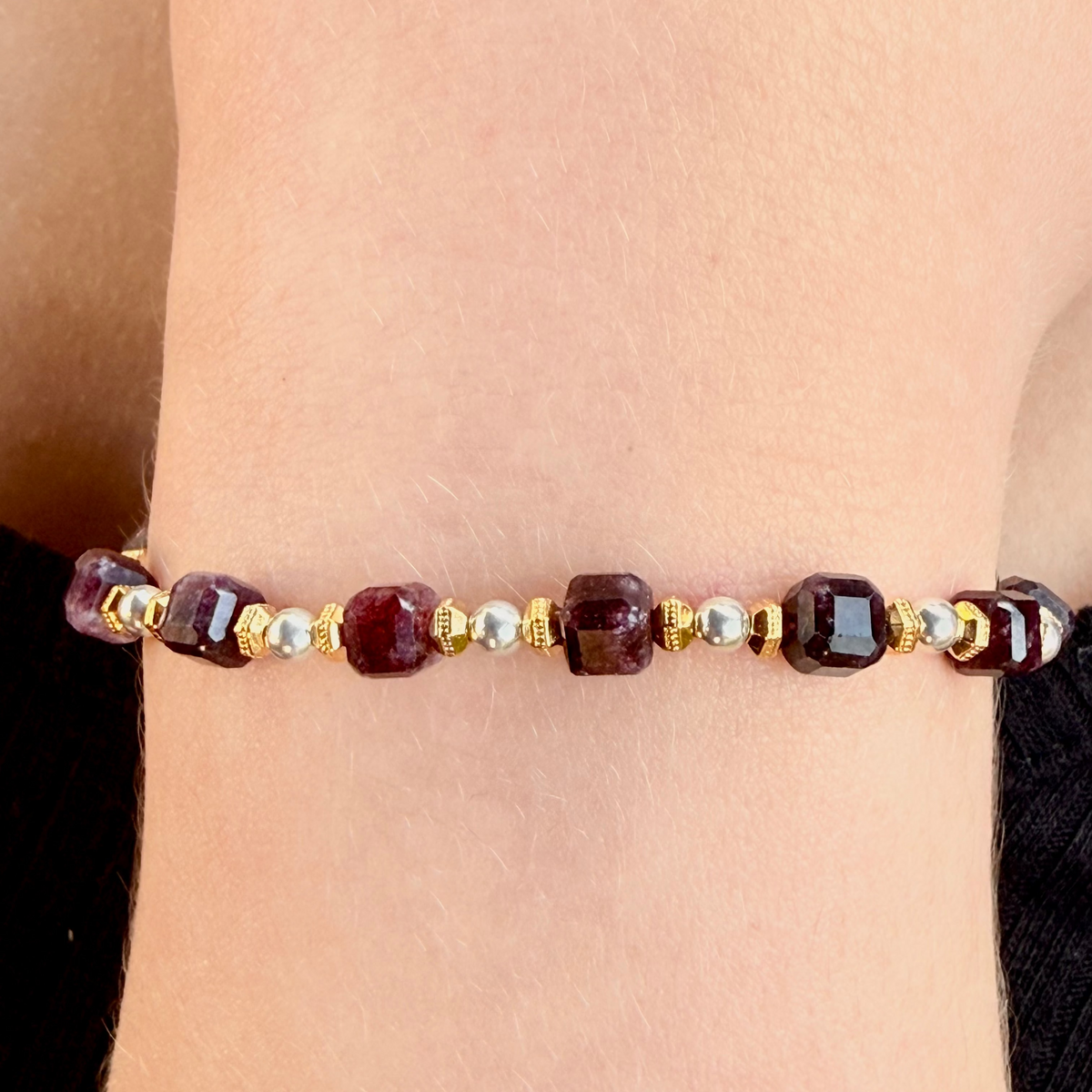 Beaded bracelet with red and gold beads on a wrist against a neutral background