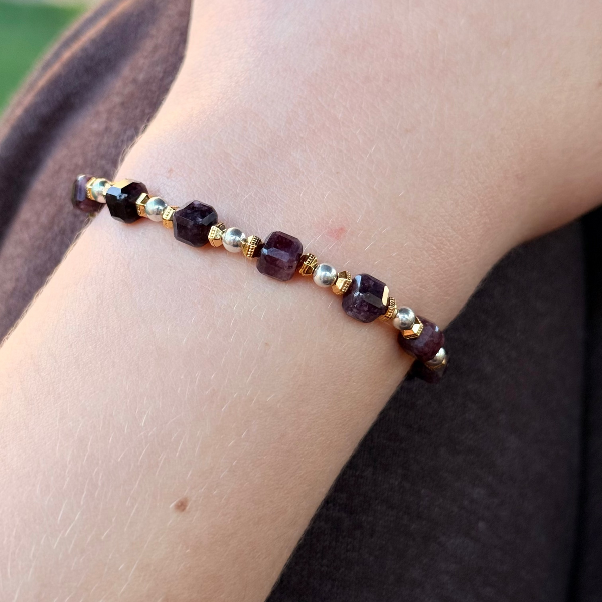 Bracelet with red and gold beads on a wrist against a blurred background