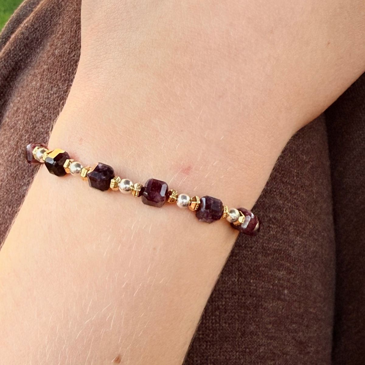 Bracelet with red and gold beads on a wrist against a brown fabric background