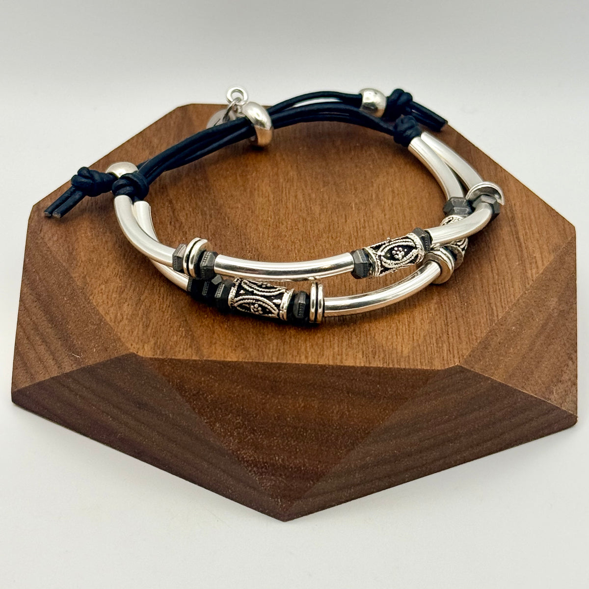 Silver bracelet with black cord on a wooden stand