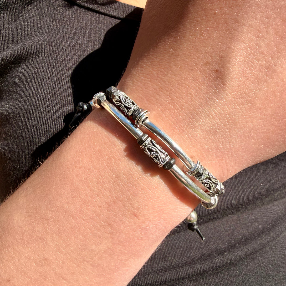 Silver bracelet with intricate designs on a wrist against a dark background