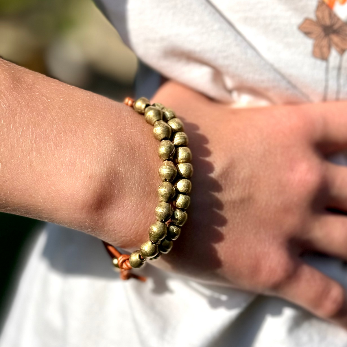 Close-up of a wrist wearing a gold beaded bracelet with a blurred background
