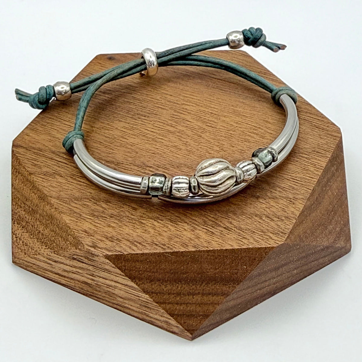 Silver bracelet with green cord on a wooden stand