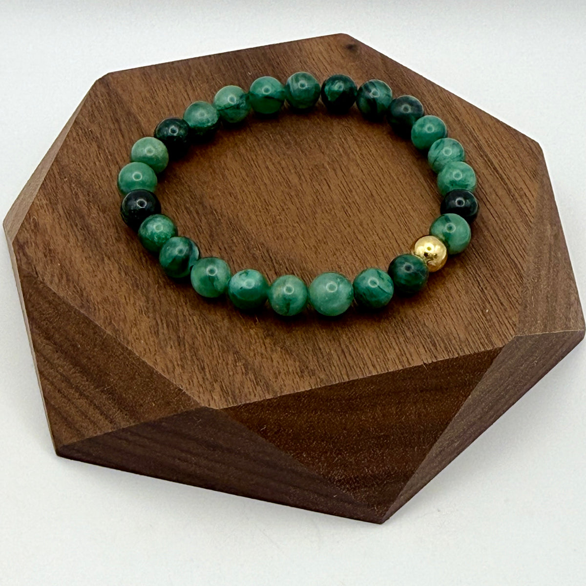 Green beaded bracelet with a gold accent on a wooden hexagonal stand.