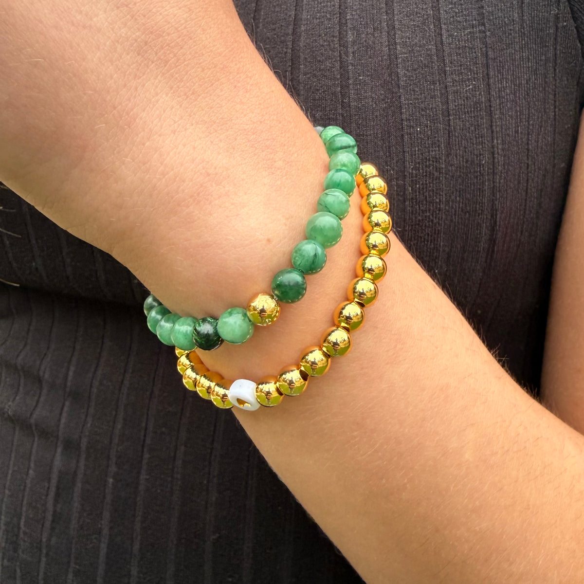 Stack of green, gold, and white beaded bracelets on a wrist against a black background