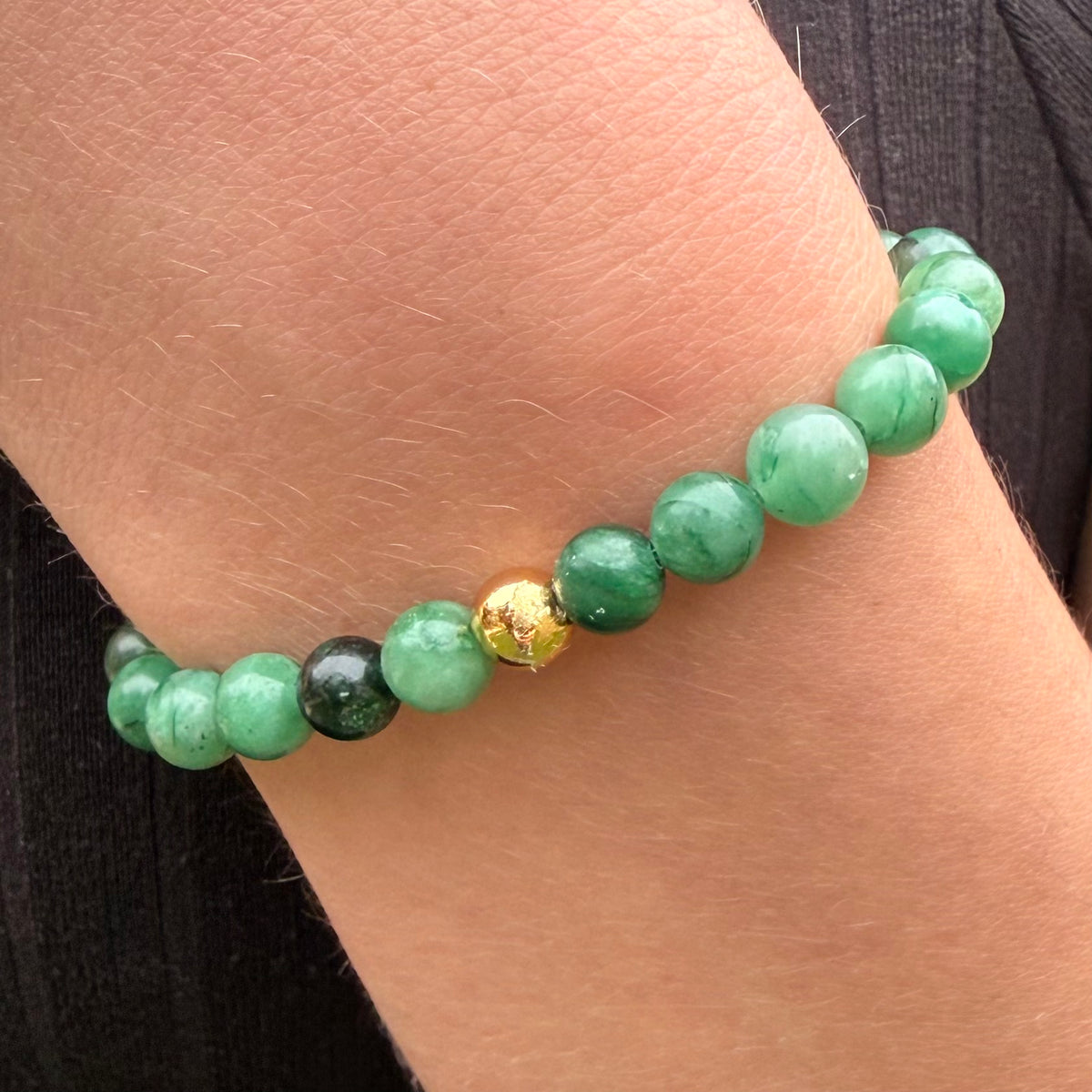 Green beaded bracelet with a gold accent on a wrist
